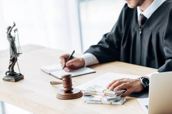 Selective focus of wooden gavel near judge writing in notebook on table — Stock Photo