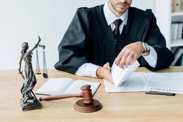 Selective focus of judge holding envelope near gavel and statuette of justice — Stock Photo