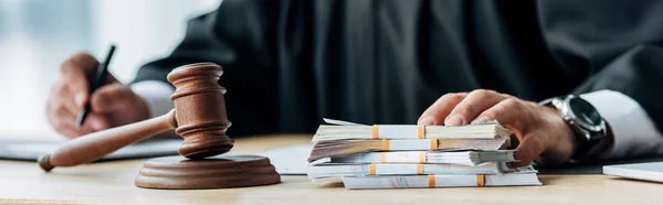 Panoramic shot of judge touching money near wooden gavel — Stock Photo