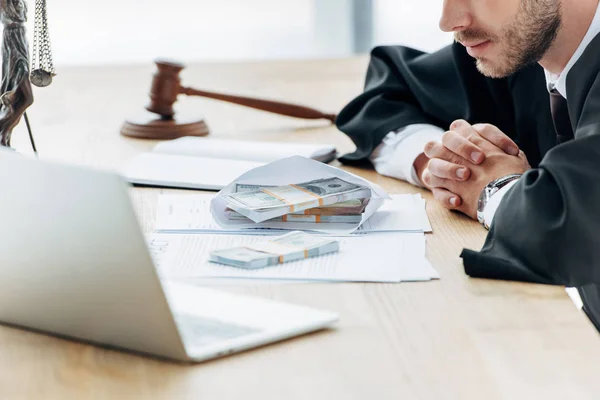 Cropped view of judge with clenched hands near money in envelope and wooden gavel — Stock Photo