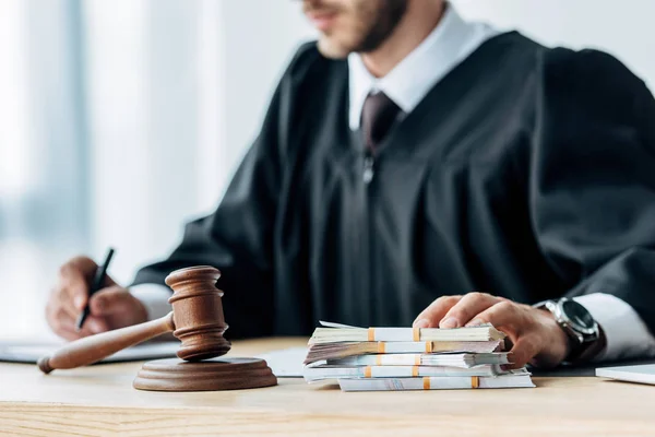 Cropped view of judge touching money near wooden gavel — Stock Photo
