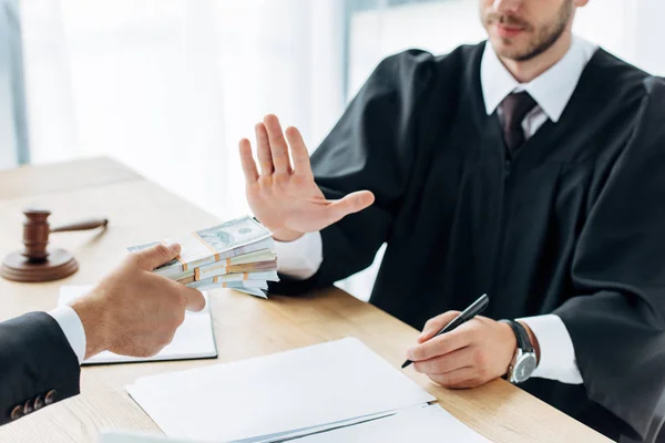 Vue recadrée de l'homme tenant de l'argent près du juge gestuelle près de la table — Photo de stock