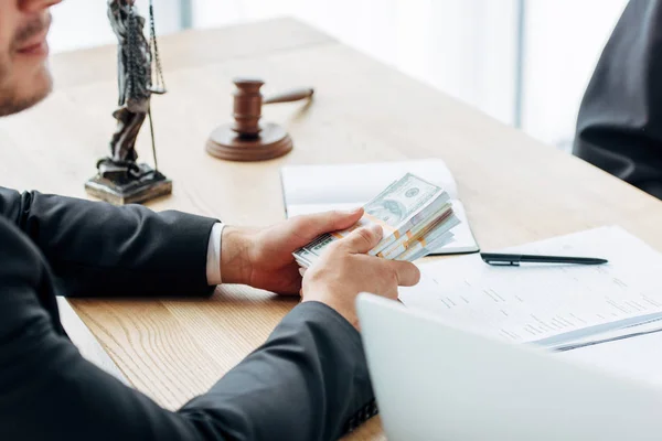 Cropped view of man holding money while sitting near wooden judge gavel — Stock Photo