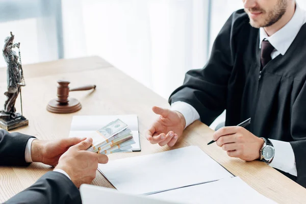 Vista recortada del hombre dando dinero para juzgar sentado cerca de la mesa - foto de stock