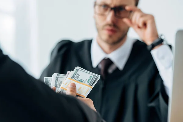 Selective focus of man holding dollar banknotes near judge in glasses — Stock Photo