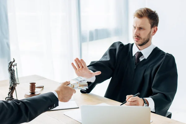 Cropped view of man holding money to displeased judge gesturing in office — Stock Photo