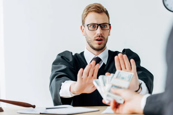 Cropped view of man holding money near surprised judge in glasses gesturing in office — Stock Photo