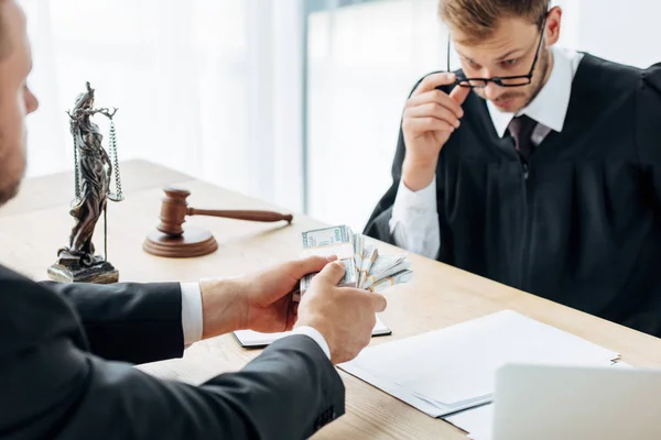 Selective focus of man holding money near handsome judge in glasses — Stock Photo
