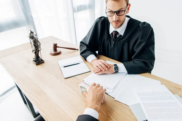 Cropped view of man holding dollar banknotes near judge in glasses — Stock Photo