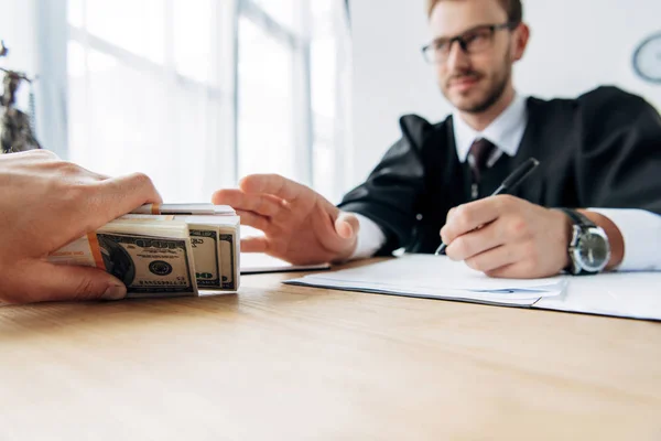 Vista recortada del hombre dando dinero en efectivo a juez feliz en gafas - foto de stock