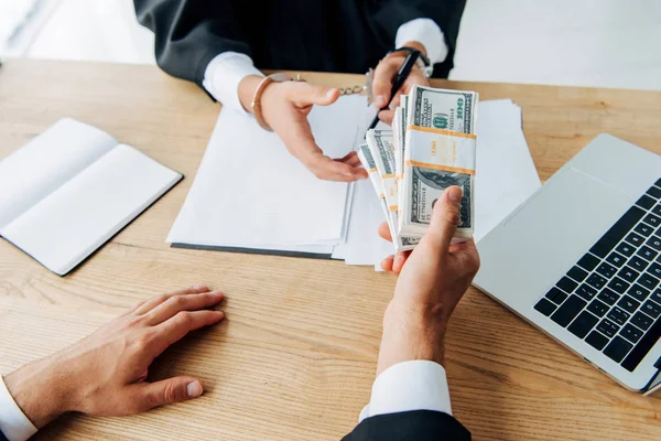 Cropped view of judge taking bribe near man sitting in office — Stock Photo