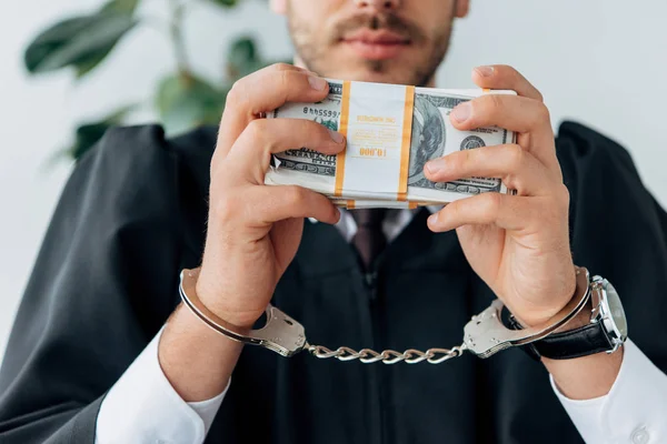 Обрізаний вид в наручниках суддя, що тримає доларові банкноти — стокове фото