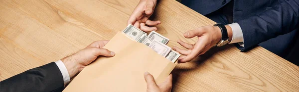 Panoramic shot of man giving envelope with bribe to judge near wooden table — Stock Photo