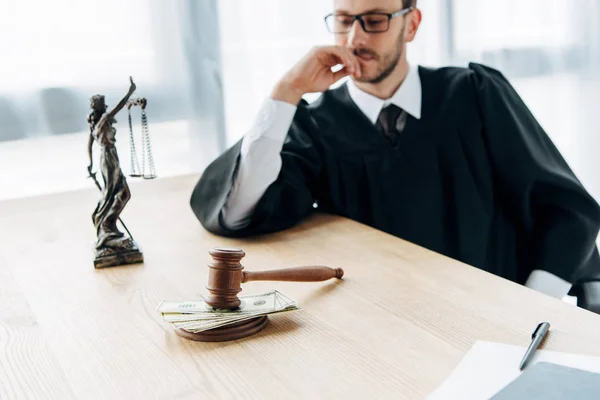 Enfoque selectivo de mazo con soborno y estatuilla de justicia cerca de juez en gafas - foto de stock