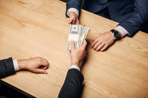 Vista superior hombre dando soborno a socio de negocios cerca de mesa de madera - foto de stock