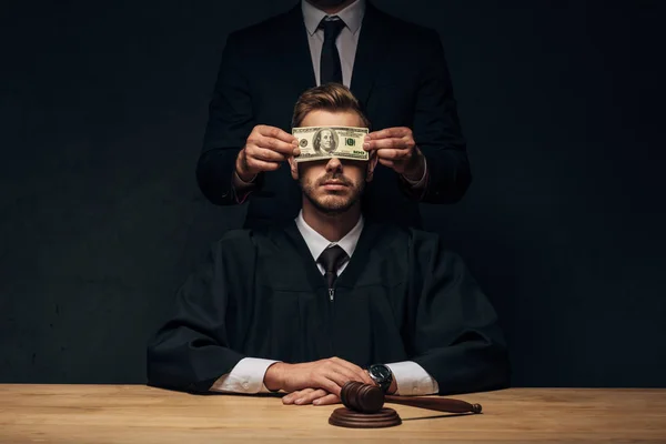 Vista recortada del hombre cubriendo la cara del juez con dinero en negro - foto de stock