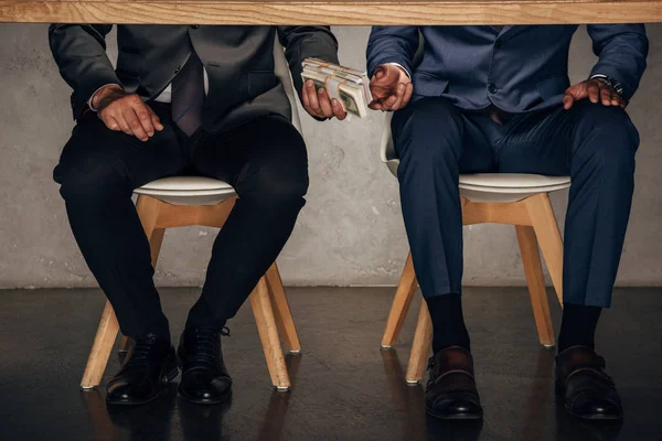Homem vista cortada dando dinheiro ao parceiro de negócios enquanto sentado na cadeira — Fotografia de Stock