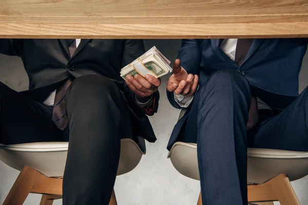 Ponto de vista cortado empresário dando suborno ao parceiro de negócios enquanto sentado na cadeira — Fotografia de Stock