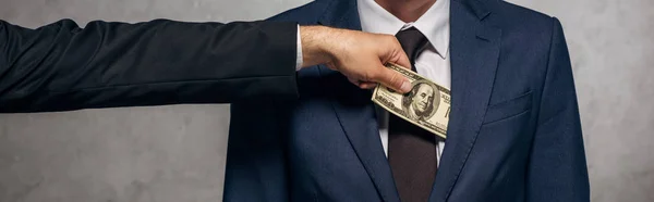 Colpo panoramico di uomo che mette contanti in tasca di socio d'affari su grigio — Foto stock