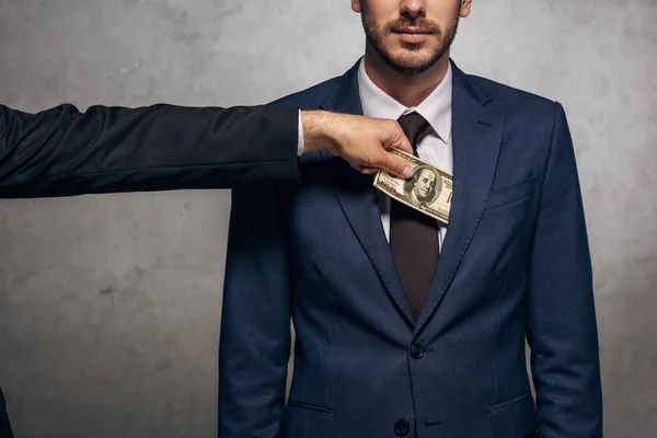 Recortado vista de hombre poniendo soborno en bolsillo de socio de negocios en gris - foto de stock