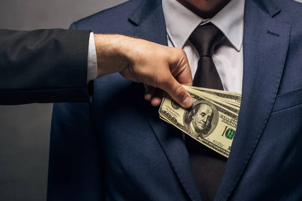 Vista ritagliata dell'uomo che mette contanti in tasca del socio d'affari su grigio — Foto stock