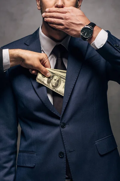 Abgeschnittene Ansicht eines Mannes, der Geld in die Tasche seines Geschäftspartners steckt und sein Gesicht auf Grau verhüllt — Stockfoto