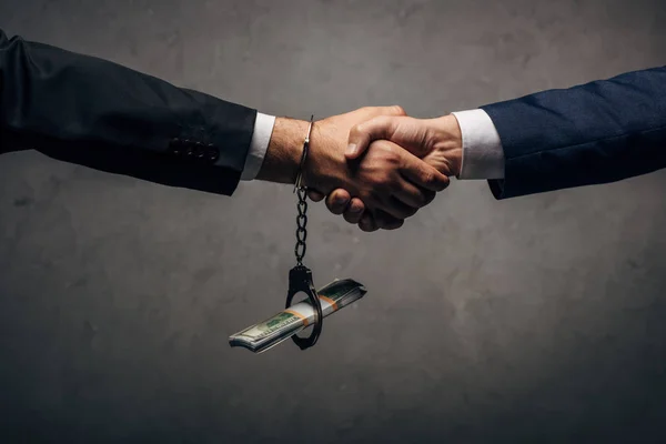Mann in Handschellen beim Händeschütteln mit Geschäftspartner auf grau — Stockfoto
