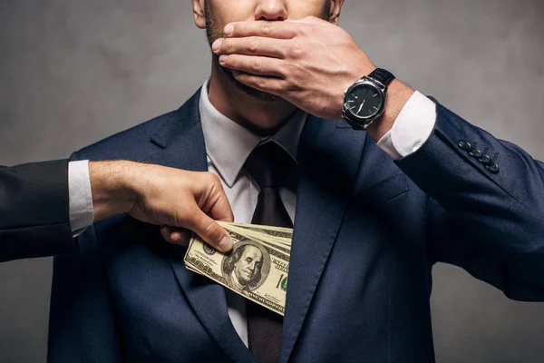 Ausgeschnittene Ansicht eines Mannes, der Bargeld in die Tasche eines Geschäftsmannes steckt und sein Gesicht auf Grau verhüllt — Stockfoto