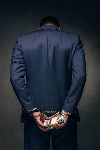 Back view of handcuffed man in suit holding bribe on grey — Stock Photo