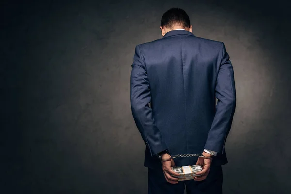Вид ззаду в наручниках чоловік у костюмі тримає гроші на сірому — стокове фото
