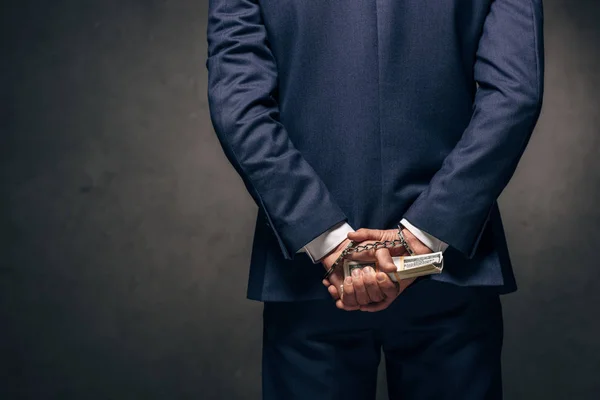 Cropped view of handcuffed man in formal wear holding bribe on grey — Stock Photo