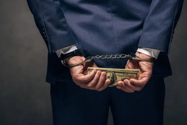 Обрезанный вид человека в наручниках, держащего взятку на сером — стоковое фото