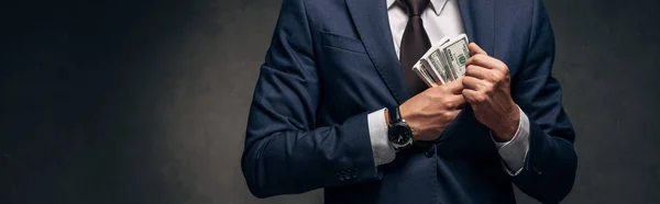 Plano panorámico de hombre de negocios en traje poniendo dinero en efectivo en el bolsillo en gris - foto de stock