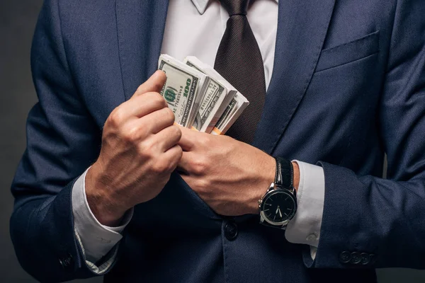 Vista recortada de hombre de negocios en traje poniendo dinero en efectivo en el bolsillo en gris - foto de stock