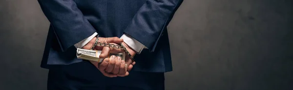 Панорамный снимок человека в наручниках, держащего взятку на сером — стоковое фото