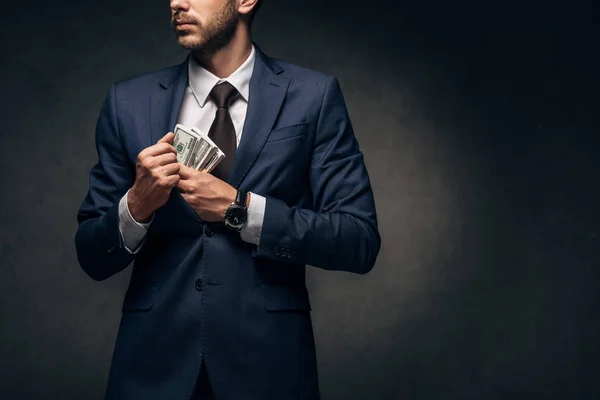 Vista recortada de hombre de negocios poniendo dinero en efectivo en el bolsillo en negro - foto de stock