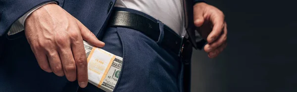 Plano panorámico de hombre de negocios poniendo dinero en efectivo en el bolsillo en gris - foto de stock