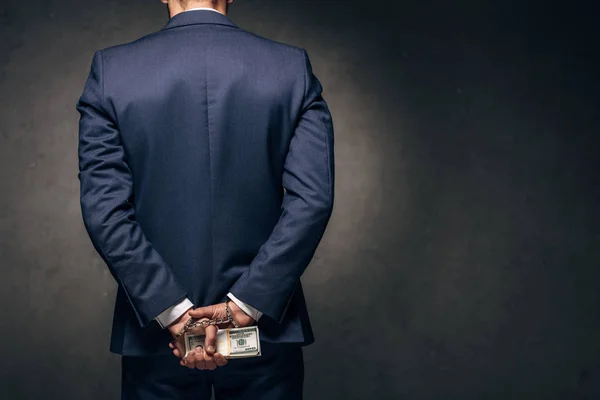 Vista posteriore di uomo ammanettato in abbigliamento formale in possesso di denaro su nero — Foto stock