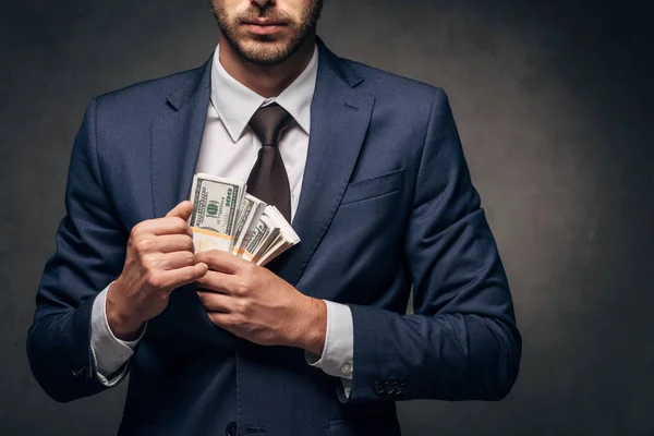 Cropped view of businessman putting bribe in pocket on black — Stock Photo