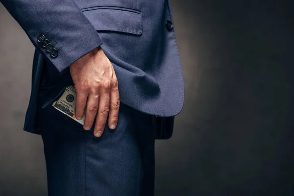 Обрізаний вид бізнесмена стоїть і кладе доларові банкноти в кишеню на сірий — стокове фото