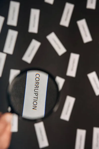 Selective focus of man holding magnifier near paper with corruption lettering on grey — Stock Photo