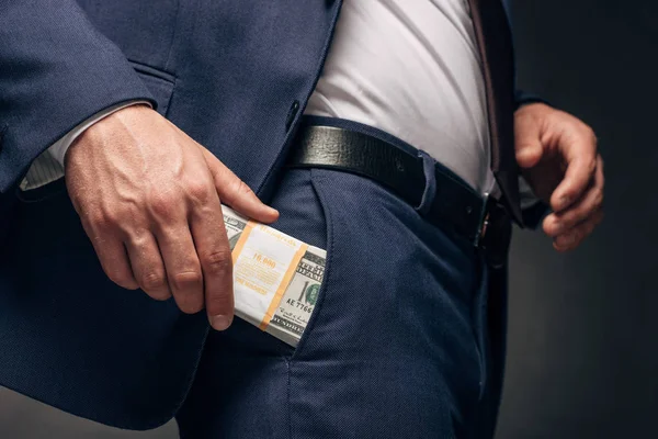 Vista recortada de hombre de negocios de pie y poner dinero en el bolsillo en gris - foto de stock