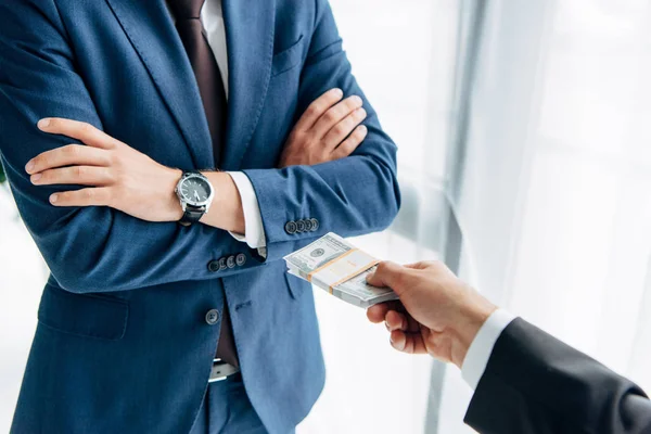 Cropped view of man giving cash to business partner standing with crossed arms on white — Stock Photo