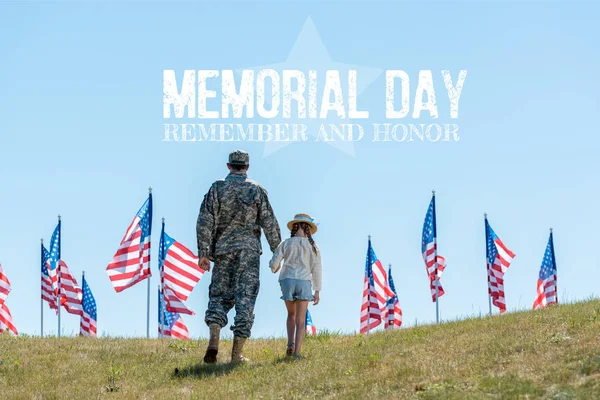 Visão traseira do pai em uniforme militar de mãos dadas com a filha perto de bandeiras americanas com ilustração do dia memorial — Fotografia de Stock