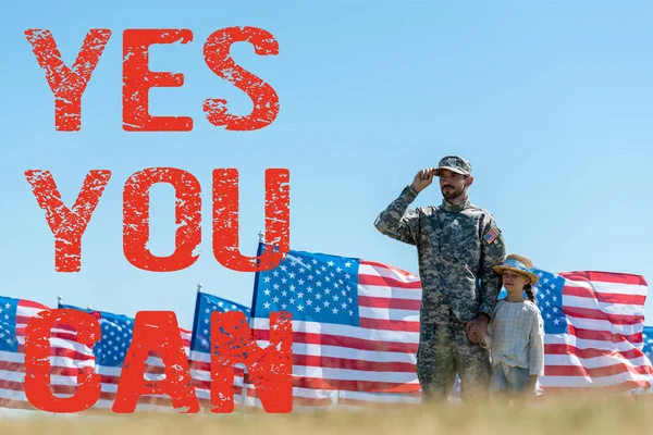 Selective focus of father in military uniform standing with cute kid near american flags with yes you can illustration — Stock Photo