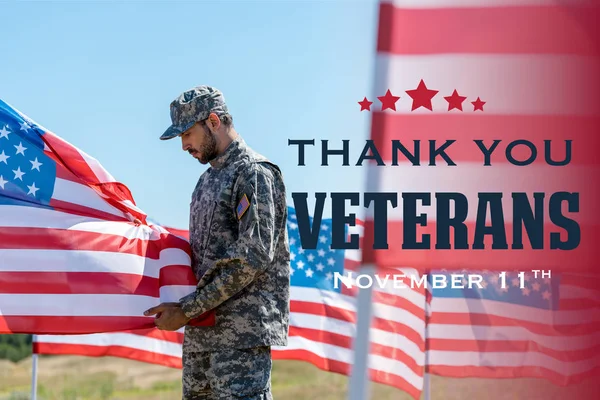 Selective focus of man in military uniform and cap standing and touching american flag  with thank you veterans illustration — Stock Photo