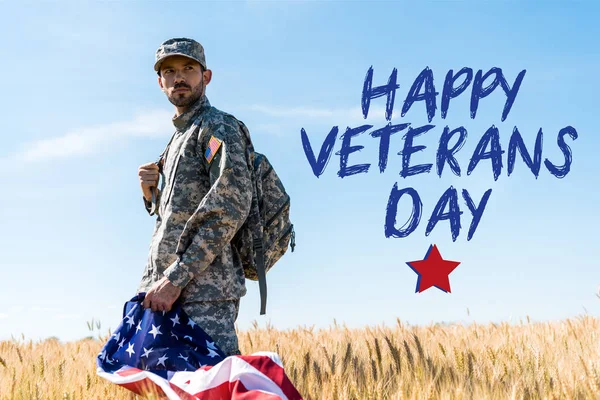 Soldier in uniform holding american flag while standing in field with happy veterans day illustration — Stock Photo