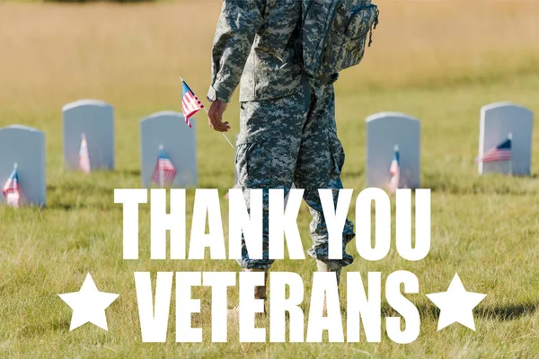 Cropped view of military man holding american flag near headstones in graveyard with thank you veterans illustration — Stock Photo