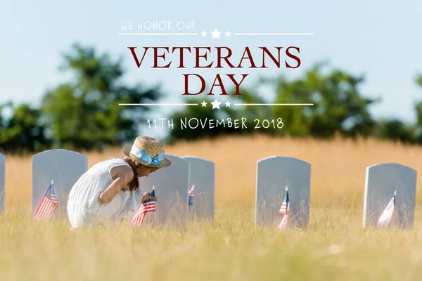 Мила дитина сидить біля надгробку з американським прапором на кладовищі з ілюстрацією дня ветеранів — стокове фото