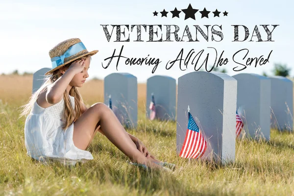 Kid in straw hat giving salute while sitting near headstones with american flags with veterans day, honoring all who served illustration — Stock Photo
